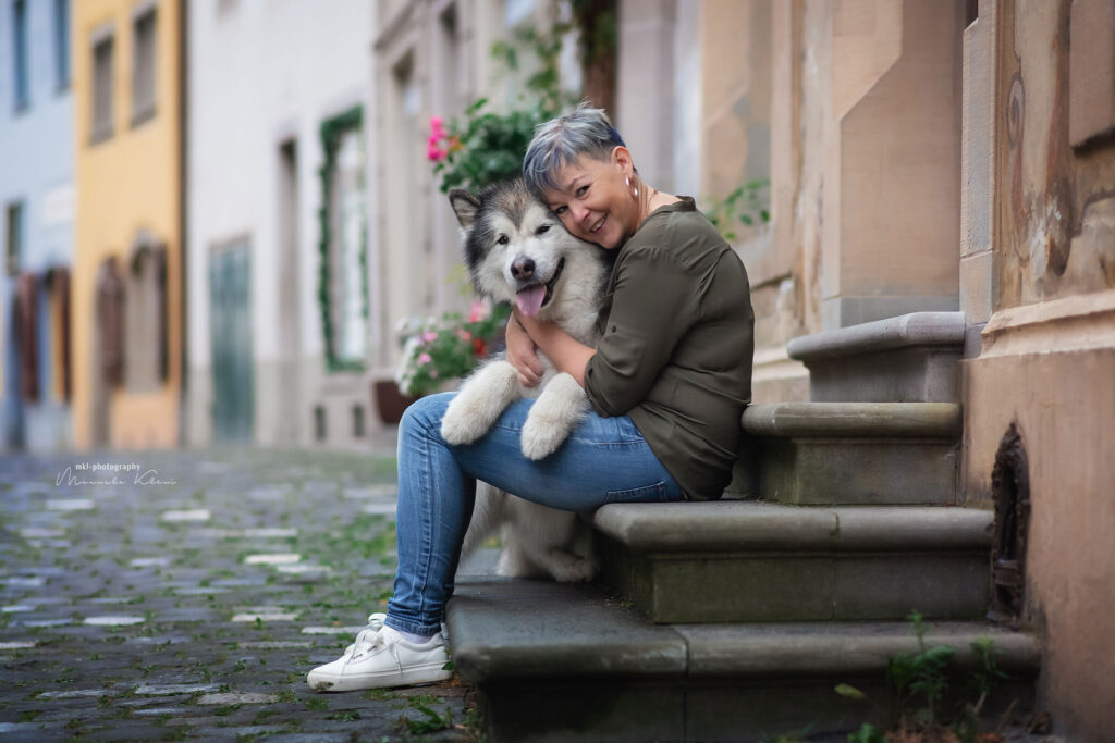Inniger Moment zwischen Frau und Malamute – Umarmung auf der Haustreppe