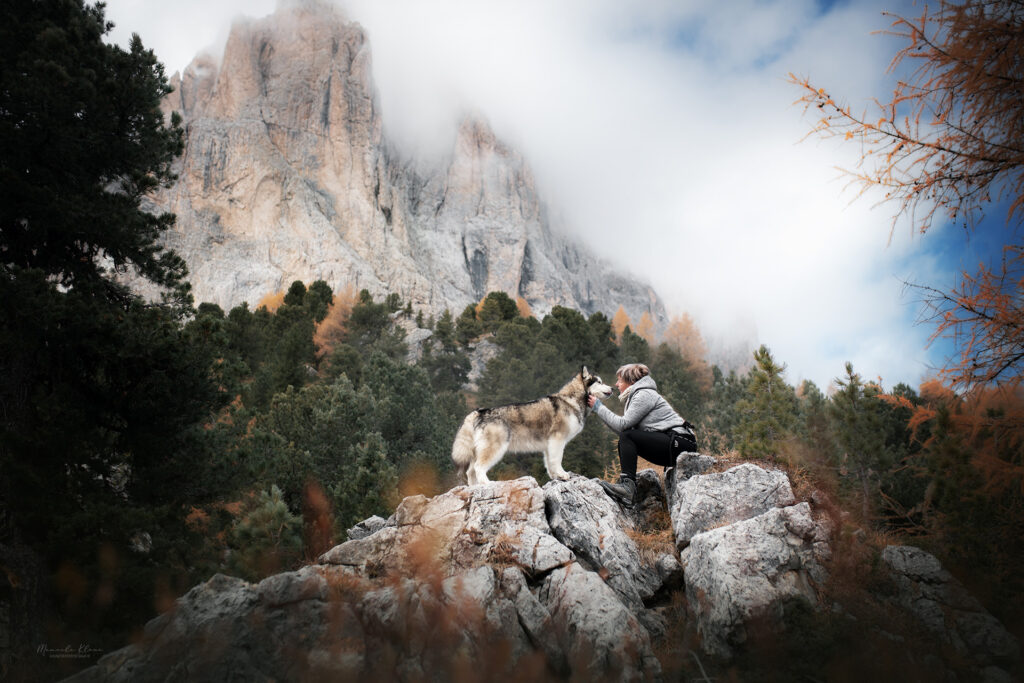 Frau mit Hund beim Wandern vor einer eindrücklichen Bergkulisse im Herbst