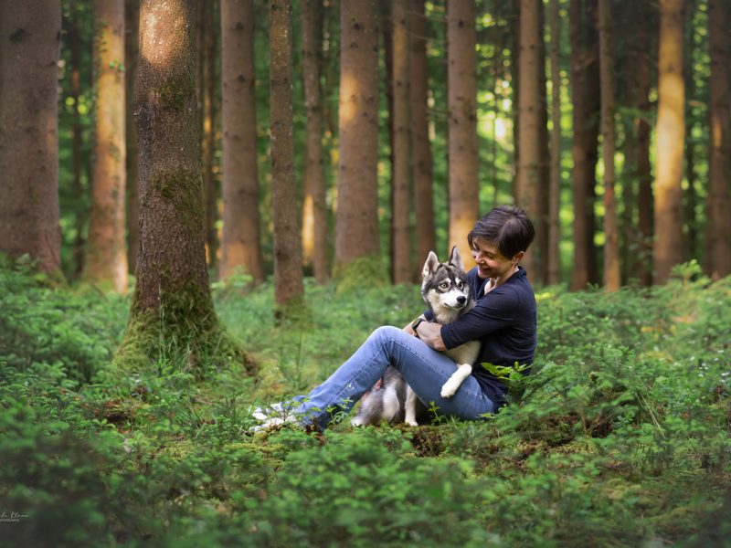 Hundefotografin Manuela Klaeui und Huendin Aberlour sitzen auf Waldboden und kuscheln