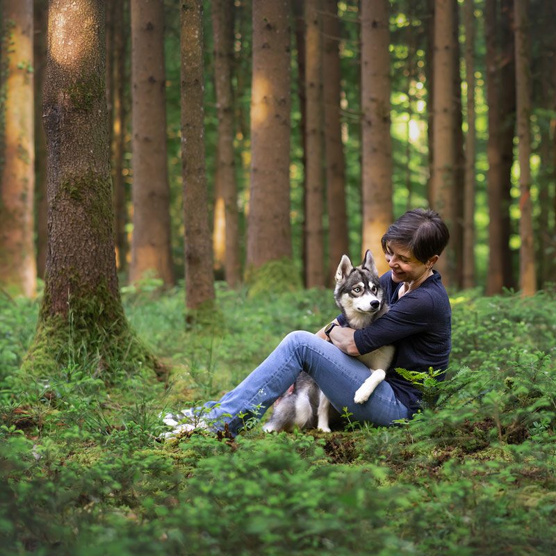 Hundefotografin Manuela Klaeui und Huendin Aberlour sitzen auf Waldboden und kuscheln